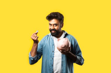 Hintli genç sakallı adam kumbarayı sarı arka planda tutuyor - insanlar ve finans kavramı
