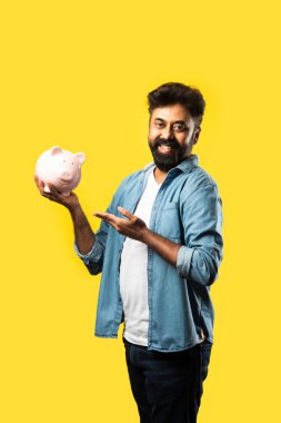 Hintli genç sakallı adam kumbarayı sarı arka planda tutuyor - insanlar ve finans kavramı