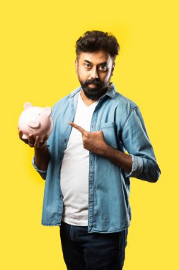 Hintli genç sakallı adam kumbarayı sarı arka planda tutuyor - insanlar ve finans kavramı