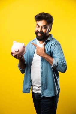 Hintli genç sakallı adam kumbarayı sarı arka planda tutuyor - insanlar ve finans kavramı
