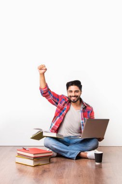 Hint üniversitesi ya da üniversite öğrencisi elinde dizüstü bilgisayarla tahta zeminde beyaz arka plana karşı kitaplar ile oturuyor.