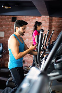 Hintli çekici çift fitness merkezinde ya da spor salonunda kardiyo eğitimi yapıyor, seçici odaklar - sağlık ve fitness konsepti