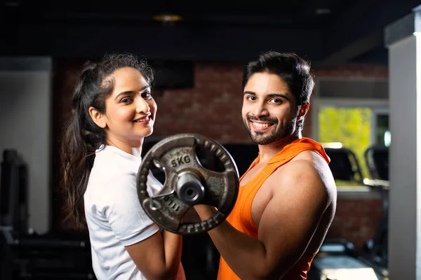 Indian asian Young couple is working out in the gym. Attractive woman and handsome fit man are training in modern gym - health and fitness concept