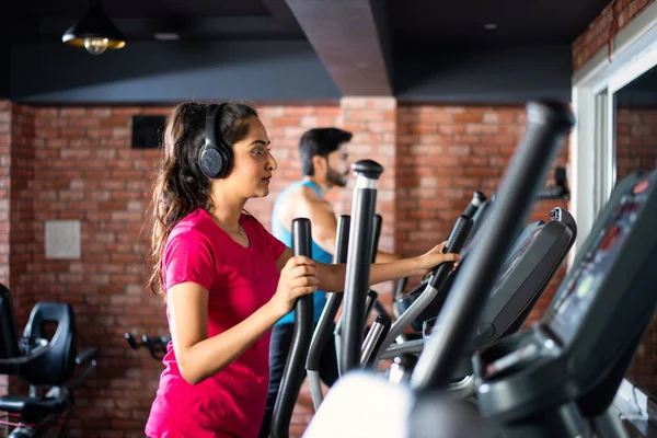 Indian asian attractive couple doing cardio training program in fitness center or gym, selective focys - health and fitness concept