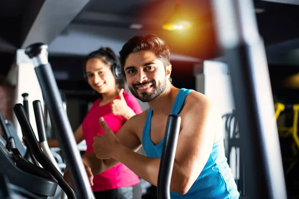 Indian asian attractive couple doing cardio training program in fitness center or gym, selective focys - health and fitness concept