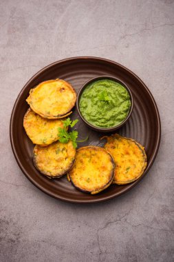 Tasty Brinjal Pakora or crispy eggplant fritters, Indian tea time snack served with green chutney clipart