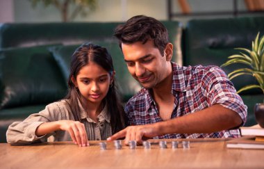 Bozuk para kulesi yapmak, Hintli baba-kız kaynaşması modern evdeki masada madeni paraları üst üste istiflemek, Asyalı baba genç kıza finansal birikimleri öğretmek, aile içi aktiviteleri öğrenmek