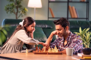 Birlikte satranç oynuyorlar, Hintli baba ve kız evde oturuyor, Asyalı baba oyun masasında genç kızla bağ kuruyor, aile kalitesi, öğrenme stratejisi, konsantrasyon ve eğlence.