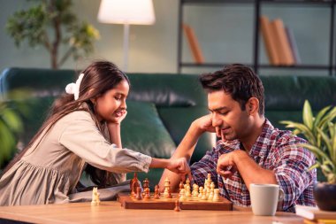 Birlikte satranç oynuyorlar, Hintli baba ve kız evde oturuyor, Asyalı baba oyun masasında genç kızla bağ kuruyor, aile kalitesi, öğrenme stratejisi, konsantrasyon ve eğlence.