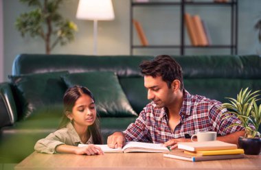 Bir ders kitabından kızı eğitmek, Hintli genç bir baba, modern evdeki masada birlikte otururken çocuk eğitimine yardım etmek, Asyalı bir baba, ev ödevi, aile bağı ve eğitimi olan bir kıza rehberlik etmek.