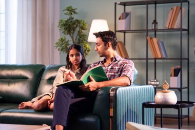 Kızına kitap okuyor, Hintli baba ve kızı modern evdeki koltukta oturuyor, Asyalı baba genç kızla bağ kuruyor, hikayeyi paylaşıyor, aile kalitesi, ev içi öğrenme ve duyguları paylaşıyor.