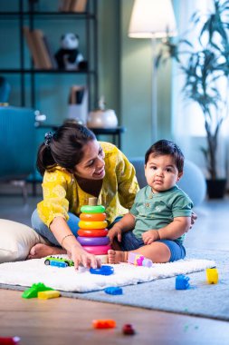 Hintli çocuk modern oturma odasında halıda otururken genç anneyle yüzük oyuncakları oynuyor. Sevgi, şefkat, bağ ve ebeveynliğin mutluluğunu paylaşıyor.