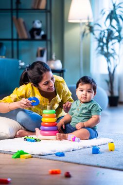 Hintli çocuk modern oturma odasında halıda otururken genç anneyle yüzük oyuncakları oynuyor. Sevgi, şefkat, bağ ve ebeveynliğin mutluluğunu paylaşıyor.