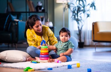 Hintli çocuk modern oturma odasında halıda otururken genç anneyle yüzük oyuncakları oynuyor. Sevgi, şefkat, bağ ve ebeveynliğin mutluluğunu paylaşıyor.