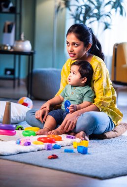 Hintli çocuk modern oturma odasında halıda otururken genç anneyle yüzük oyuncakları oynuyor. Sevgi, şefkat, bağ ve ebeveynliğin mutluluğunu paylaşıyor.