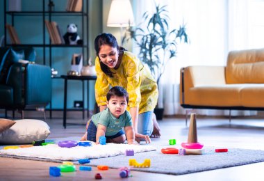 Hintli çocuk halıda genç annesiyle birlikte modern oturma odasında sürünüyor, neşeli anları paylaşıyor, sevgi, şefkat, bağ kurma ve erken çocukluk gelişimini evde besliyor.