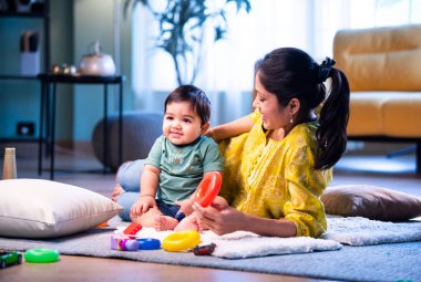 Hintli çocuk modern oturma odasında halıda otururken genç anneyle yüzük oyuncakları oynuyor. Sevgi, şefkat, bağ ve ebeveynliğin mutluluğunu paylaşıyor.