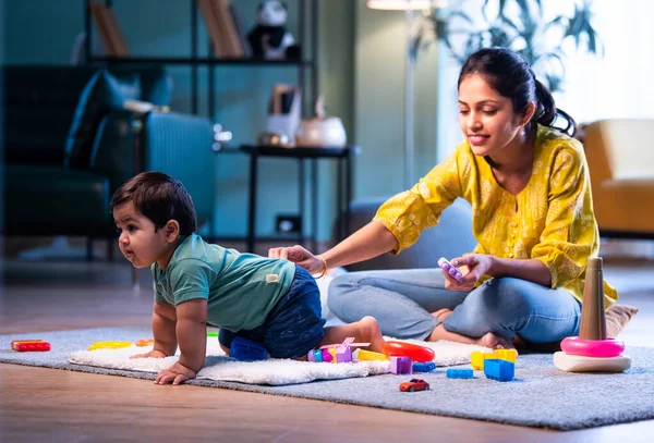 Hintli çocuk halıda genç annesiyle birlikte modern oturma odasında sürünüyor, neşeli anları paylaşıyor, sevgi, şefkat, bağ kurma ve erken çocukluk gelişimini evde besliyor.
