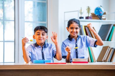 Sınıfta üniforma giyerek Tiffin yiyen ve paylaşan Hintli okul çocukları, okul günü boyunca arkadaşlarıyla keyifli ve samimi bir çocukluk anıyla öğle yemeği molasının tadını çıkarıyorlar.