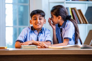 Okul üniformalarını giyerken arkadaşlarıyla dedikodu yapan, gizli konuşmalar yapan ve okuldaki çalışma saatleri arasında sessizce gülen Hintli okul çocukları.