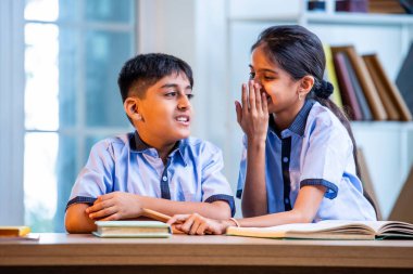 Okul üniformalarını giyerken arkadaşlarıyla dedikodu yapan, gizli konuşmalar yapan ve okuldaki çalışma saatleri arasında sessizce gülen Hintli okul çocukları.