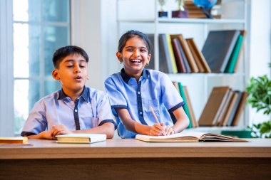 Hintli okul çocukları okul üniformalarını giyerken yüksek sesle gülüyorlar, birlikte neşeli bir anın tadını çıkarıyorlar, akademik tatilde kahkahalarla neşe ve bağ kuruyorlar.