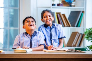 Hintli okul çocukları okul üniformalarını giyerken yüksek sesle gülüyorlar, birlikte neşeli bir anın tadını çıkarıyorlar, akademik tatilde kahkahalarla neşe ve bağ kuruyorlar.