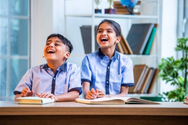 Hintli okul çocukları okul üniformalarını giyerken yüksek sesle gülüyorlar, birlikte neşeli bir anın tadını çıkarıyorlar, akademik tatilde kahkahalarla neşe ve bağ kuruyorlar.