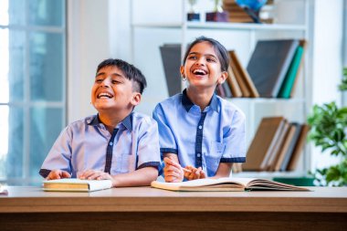 Hintli okul çocukları okul üniformalarını giyerken yüksek sesle gülüyorlar, birlikte neşeli bir anın tadını çıkarıyorlar, akademik tatilde kahkahalarla neşe ve bağ kuruyorlar.