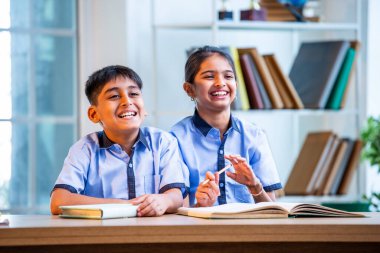 Hintli okul çocukları okul üniformalarını giyerken yüksek sesle gülüyorlar, birlikte neşeli bir anın tadını çıkarıyorlar, akademik tatilde kahkahalarla neşe ve bağ kuruyorlar.