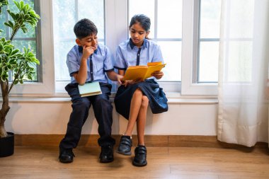 Okul üniformalarını giyerken sınıfın penceresinde oturup kitap okuyan Hintli okul çocukları akademik gün boyunca düşünceli, sessiz çalışma saatlerine gömüldüler.