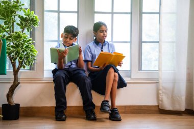 Okul üniformalarını giyerken sınıfın penceresinde oturup kitap okuyan Hintli okul çocukları akademik gün boyunca düşünceli, sessiz çalışma saatlerine gömüldüler.