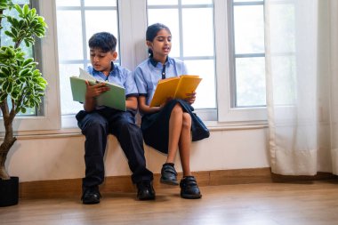 Okul üniformalarını giyerken sınıfın penceresinde oturup kitap okuyan Hintli okul çocukları akademik gün boyunca düşünceli, sessiz çalışma saatlerine gömüldüler.