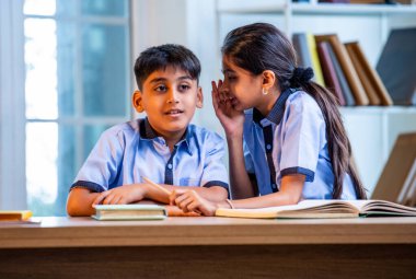 Okul üniformalarını giyerken arkadaşlarıyla dedikodu yapan, gizli konuşmalar yapan ve okuldaki çalışma saatleri arasında sessizce gülen Hintli okul çocukları.
