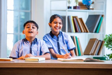 Hintli okul çocukları okul üniformalarını giyerken yüksek sesle gülüyorlar, birlikte neşeli bir anın tadını çıkarıyorlar, akademik tatilde kahkahalarla neşe ve bağ kuruyorlar.