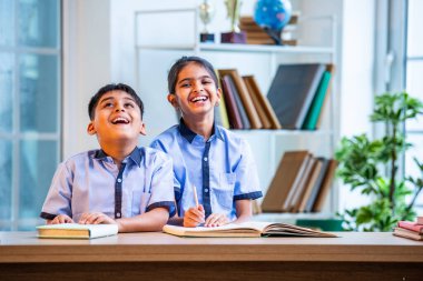 Hintli okul çocukları okul üniformalarını giyerken yüksek sesle gülüyorlar, birlikte neşeli bir anın tadını çıkarıyorlar, akademik tatilde kahkahalarla neşe ve bağ kuruyorlar.