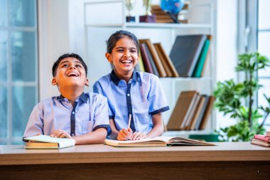 Hintli okul çocukları okul üniformalarını giyerken yüksek sesle gülüyorlar, birlikte neşeli bir anın tadını çıkarıyorlar, akademik tatilde kahkahalarla neşe ve bağ kuruyorlar.