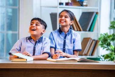 Hintli okul çocukları okul üniformalarını giyerken yüksek sesle gülüyorlar, birlikte neşeli bir anın tadını çıkarıyorlar, akademik tatilde kahkahalarla neşe ve bağ kuruyorlar.