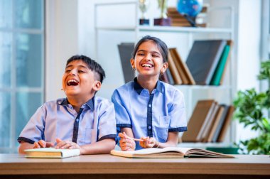 Hintli okul çocukları okul üniformalarını giyerken yüksek sesle gülüyorlar, birlikte neşeli bir anın tadını çıkarıyorlar, akademik tatilde kahkahalarla neşe ve bağ kuruyorlar.