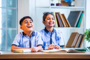 Hintli okul çocukları okul üniformalarını giyerken yüksek sesle gülüyorlar, birlikte neşeli bir anın tadını çıkarıyorlar, akademik tatilde kahkahalarla neşe ve bağ kuruyorlar.