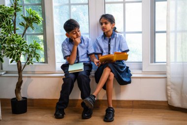 Okul üniformalarını giyerken sınıfın penceresinde oturup kitap okuyan Hintli okul çocukları akademik gün boyunca düşünceli, sessiz çalışma saatlerine gömüldüler.