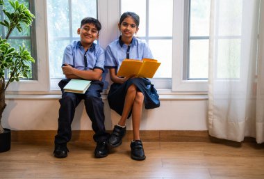 Okul üniformalarını giyerken sınıfın penceresinde oturup kitap okuyan Hintli okul çocukları akademik gün boyunca düşünceli, sessiz çalışma saatlerine gömüldüler.