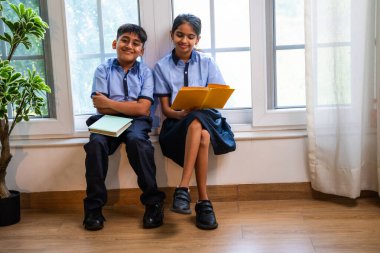 Okul üniformalarını giyerken sınıfın penceresinde oturup kitap okuyan Hintli okul çocukları akademik gün boyunca düşünceli, sessiz çalışma saatlerine gömüldüler.