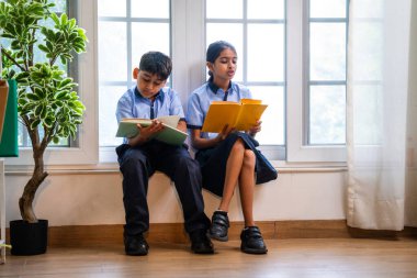 Okul üniformalarını giyerken sınıfın penceresinde oturup kitap okuyan Hintli okul çocukları akademik gün boyunca düşünceli, sessiz çalışma saatlerine gömüldüler.