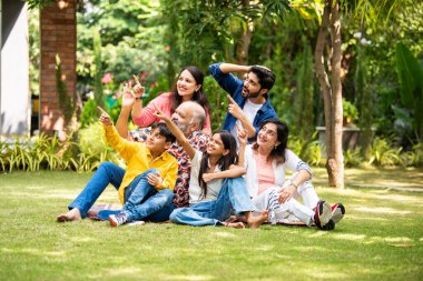 Hint çoklu nesiller ailesi yeşil çimlerin üzerinde birlikte oturan bir şeyi işaret ediyor ve altı mutlu üye bahçede oturmuş neşeli ifadeleri olan hayali bir ürün sergiliyor.