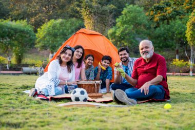Hintli aile dışarıda kamp yaparken meyve yiyor, kahkahalarla, sağlıklı atıştırmalarla, neşeli sohbetlerle ve huzurlu doğal ortamlarda neşeli birlikteliklerle rahat vakit geçiriyor.