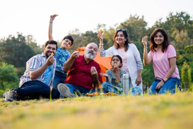 Hint ailesi dışarıda kamp yaparken abur cubur yiyor, kameraya bakıyor, neşeli bağlanma anlarının tadını çıkarıyor, kahkahaları paylaşıyor, gevşemiş sohbetler yapıyor, sıcak etkileşimler kuruyor ve birlikte keyifli güzel vakit geçiriyorlar.