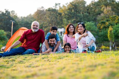 Hintli aile dışarıda kamp yaparken yalan söylüyor ve sohbet ediyor, gevşetici sohbetlerin tadını çıkarıyor, neşeli gülüşler, sıcak gülümsemeler, neşeli birliktelikler, ve doğada huzur dolu kaliteli zamanlar.