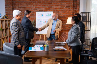 Hintli işadamları, Hindistan 'ın üst düzey Asyalı iş adamları olarak sunum yaparken el sıkışıyorlar. Yüksek yönetim, samimi modern ofis grafiği kullanarak başarılı büyüme projeksiyonunu kutluyor.