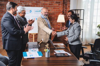 Hintli işadamları, Hindistan 'ın üst düzey Asyalı iş adamları olarak sunum yaparken el sıkışıyorlar. Yüksek yönetim, samimi modern ofis grafiği kullanarak başarılı büyüme projeksiyonunu kutluyor.